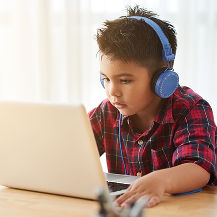 a young boy using a laptop computer sitting on top of a table